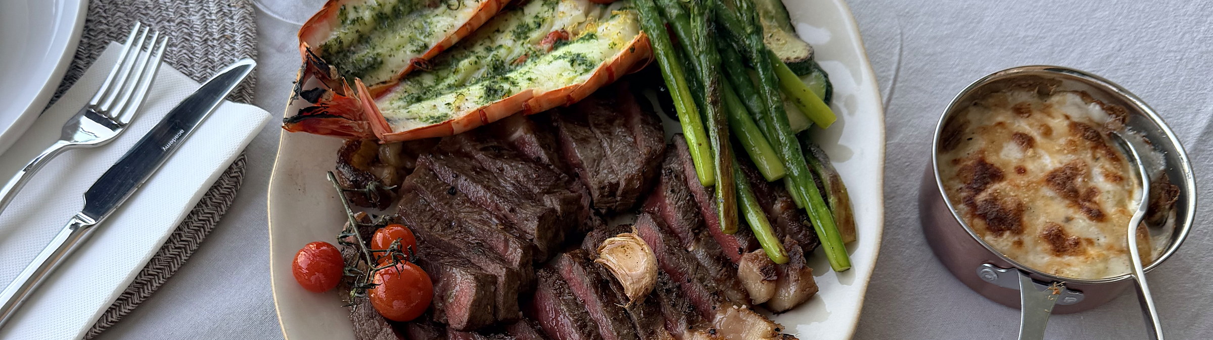 A platter of sliced steak, grilled prawns and asparagus with a gratin, served at a laid table