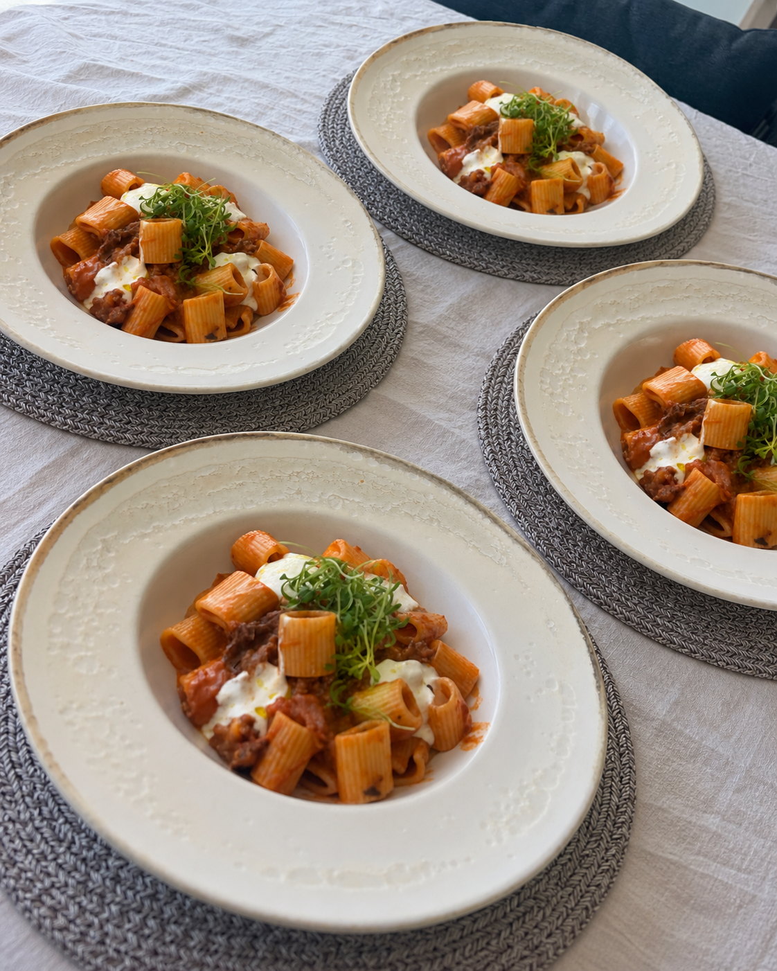 Four plates of rigatoni with ragù and burrata on a laid table