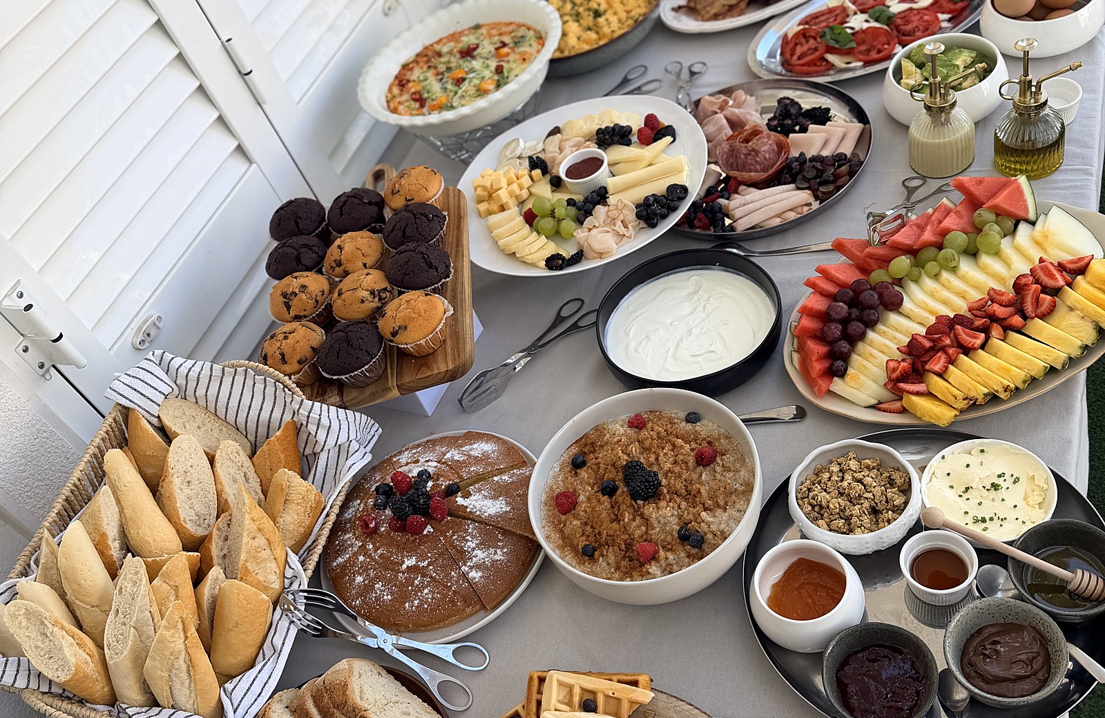 A brunch table with pastries, fruit, granola and cured meats