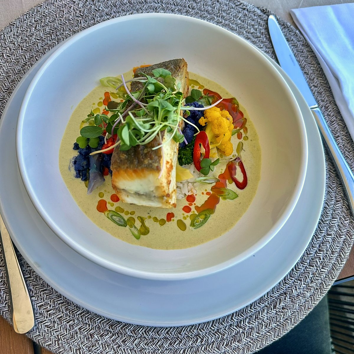 A plated fish course with a light sauce and fresh herbs