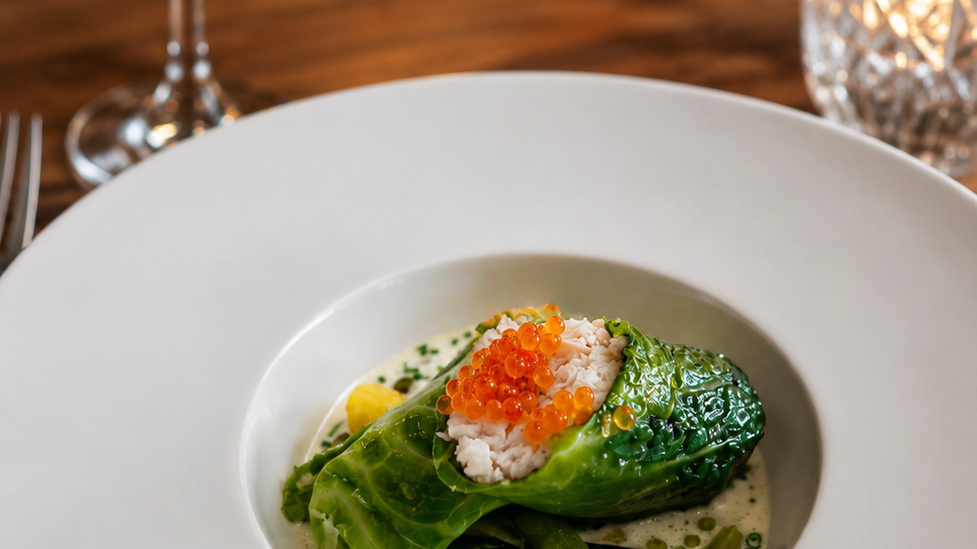 A cabbage roll filled with crab and topped with salmon roe in a white bowl